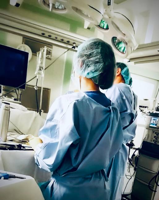 Хирургическая команда: операционная медсестра и врачи в стерильной одежде под операционными лампами в современном операционном блоке.