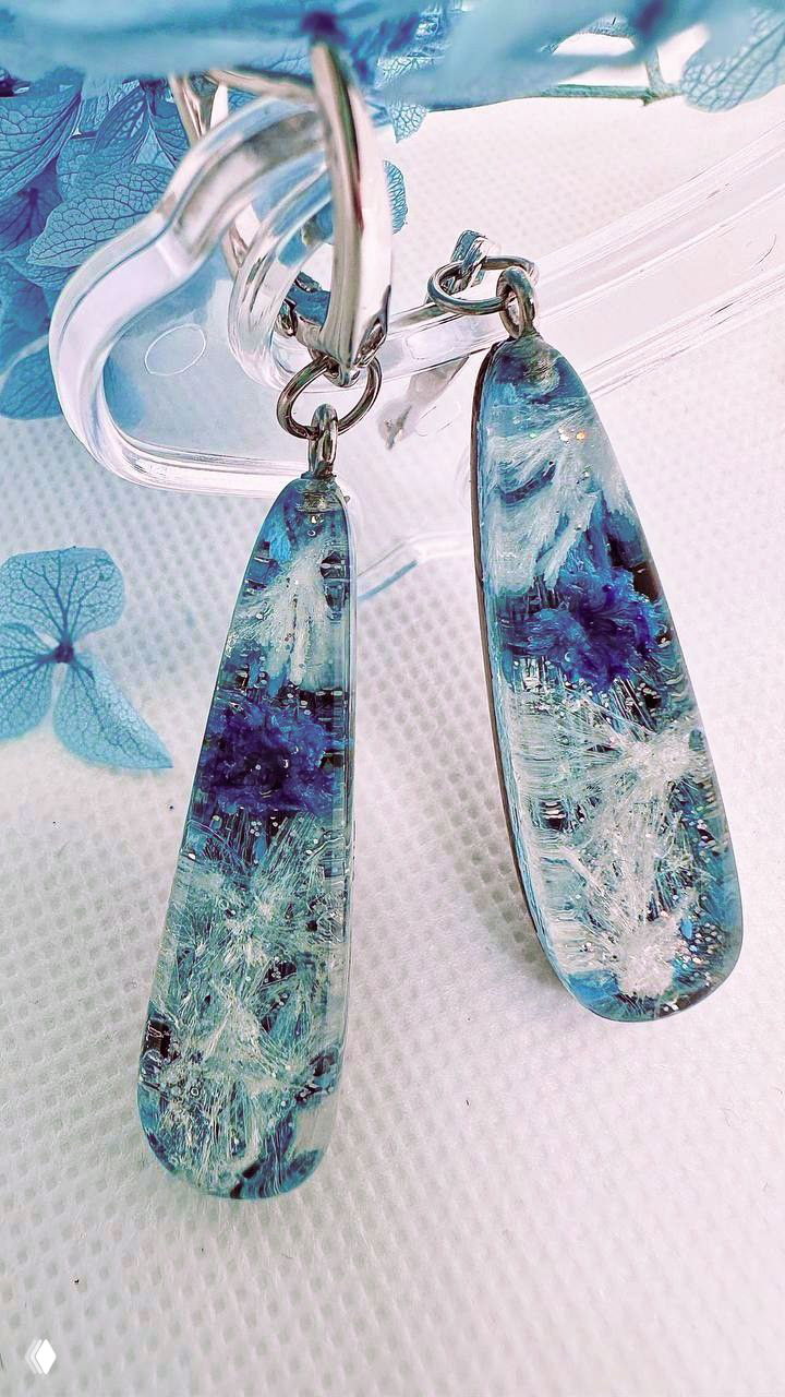 Крупный план пары серьёз из эпоксидной смолы с синими и белыми включениями, эффектом глубины и текстурой, напоминающей льдинки.