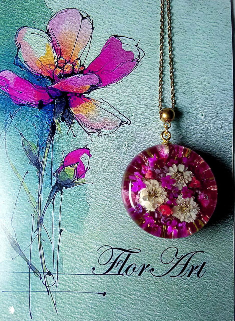 Круглый кулон с розово‑фиолетовой заливкой и белыми мини‑цветами на фоне художественной открытки — крупный план.