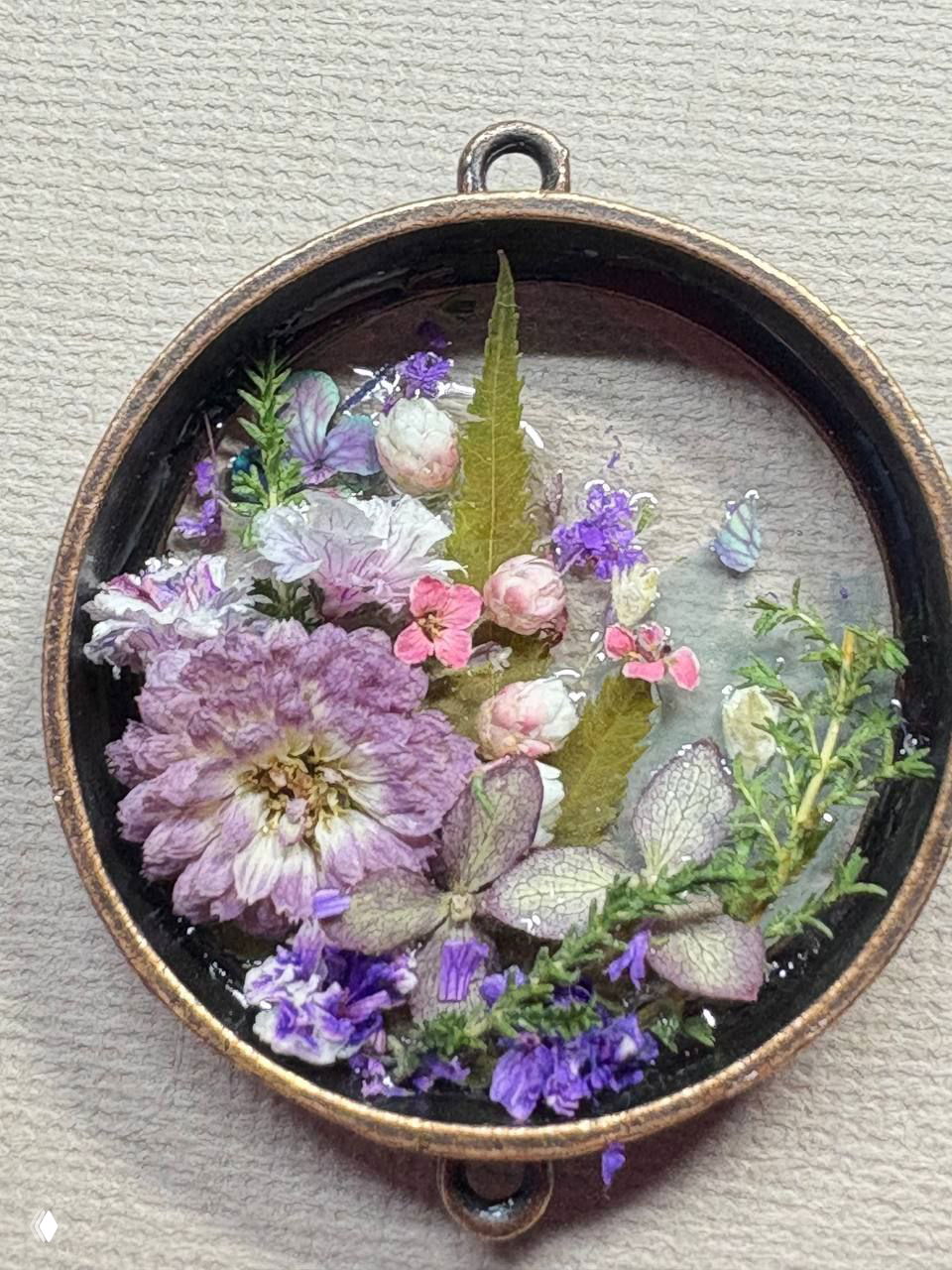 Овальный медальон с нежной сиренево‑розовой цветочной композицией, залитый в бронзовой оправе — детальный фрагмент.