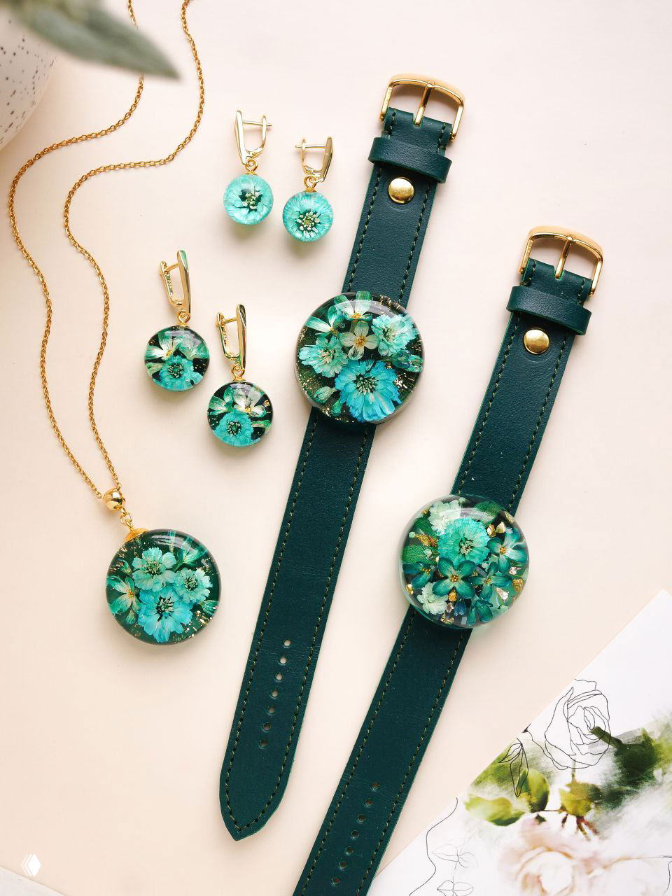 Набор зелёных украшений: две часовые застёжки с круглыми смоляными вставками и несколько серёг с бирюзовыми цветами и золотыми деталями на светлом фоне.