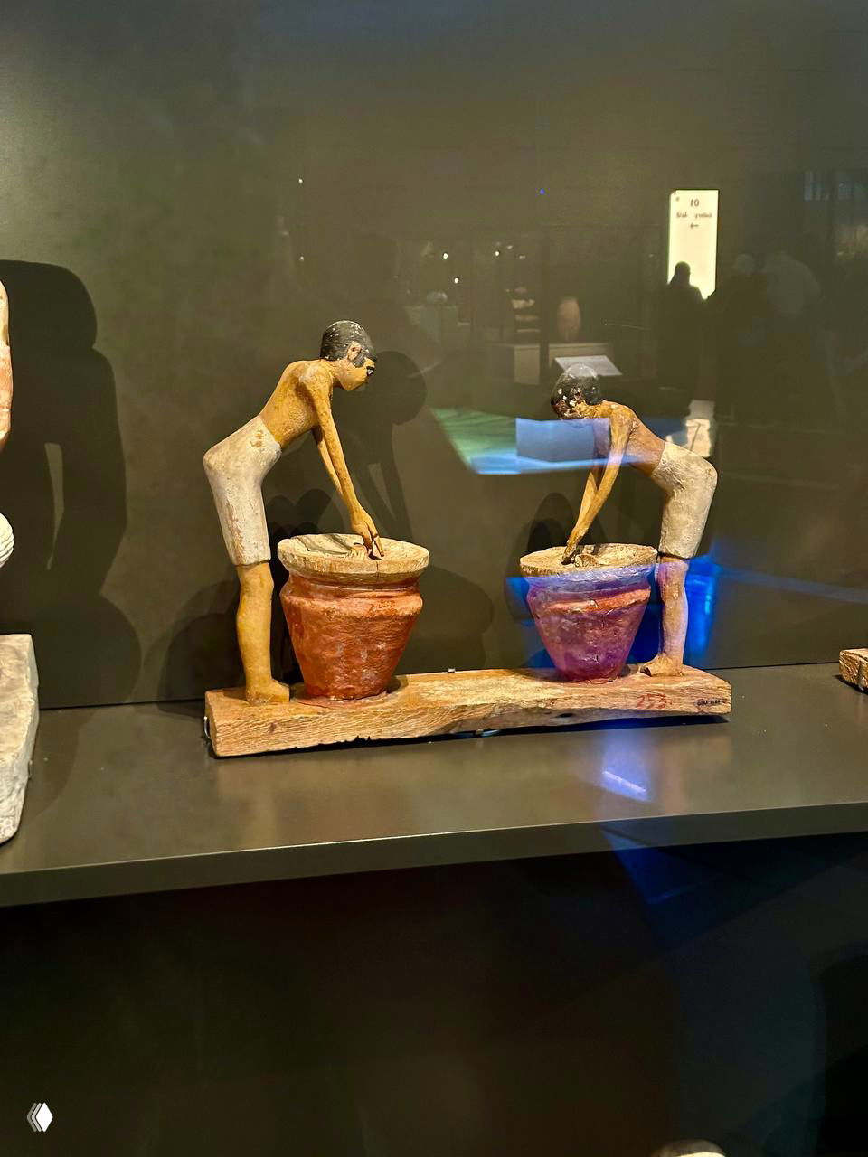 Две окрашенные деревянные фигурки, наклонённые над кадками; сцена разминания зерна и приготовления пивного сусла.