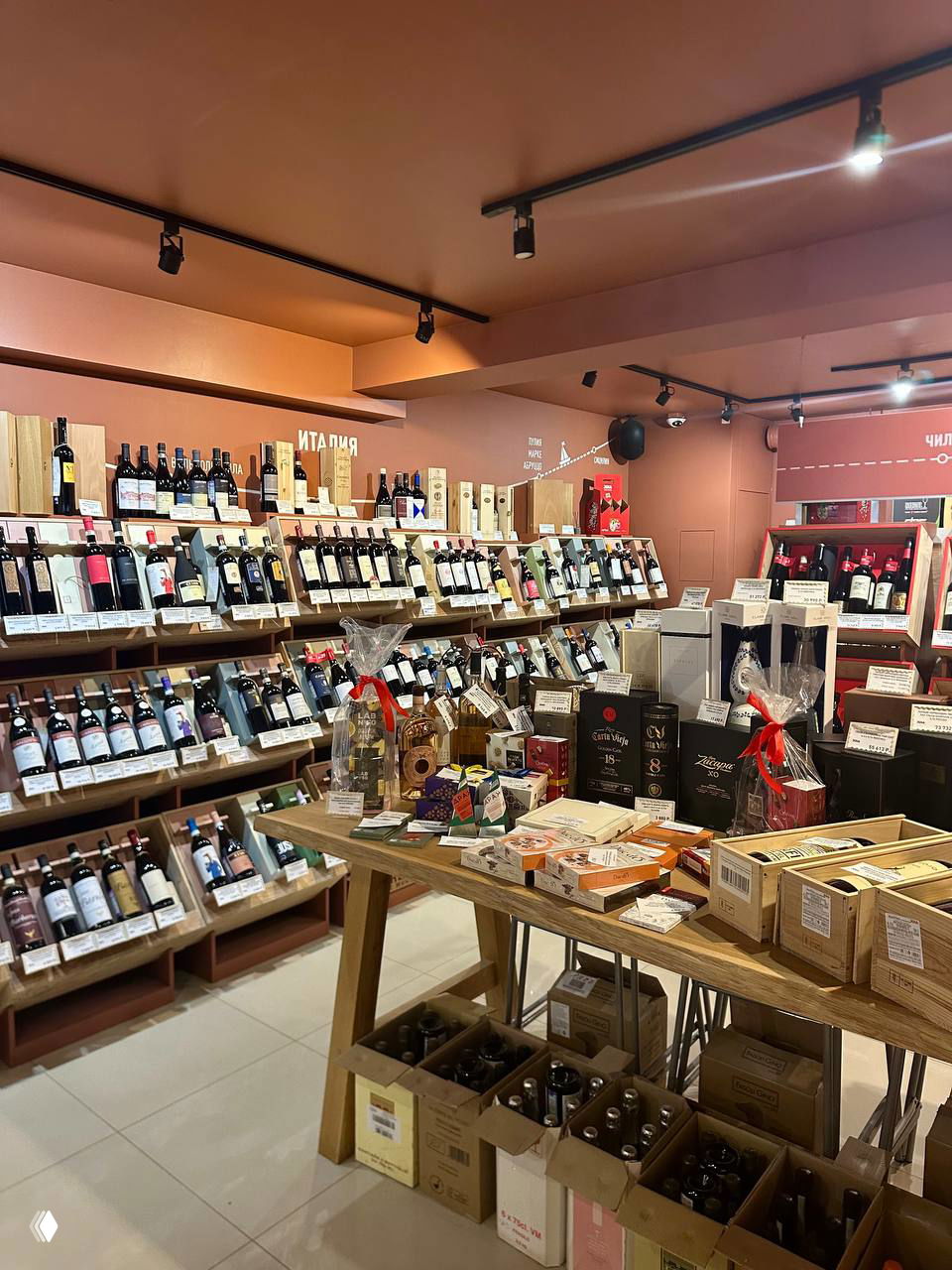 Интерьер винного магазина JOIA: деревянные стеллажи, множество бутылок на полках, центральный стол с подарочными наборами.