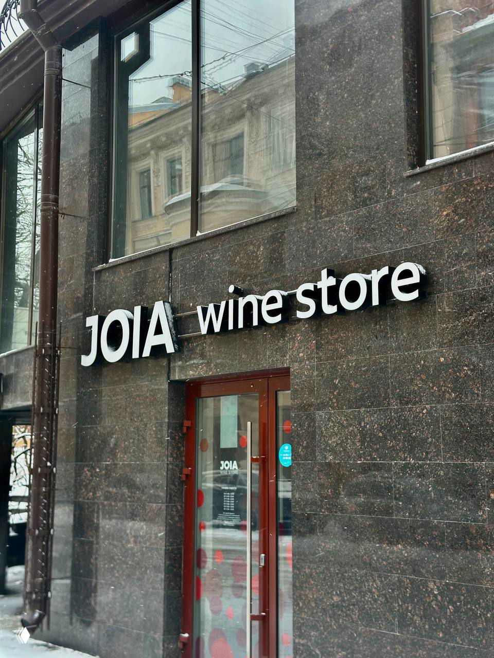 Фасад JOIA wine store на городской улице зимой: крупная вывеска, входная дверь с логотипом и отражения зданий в витрине.