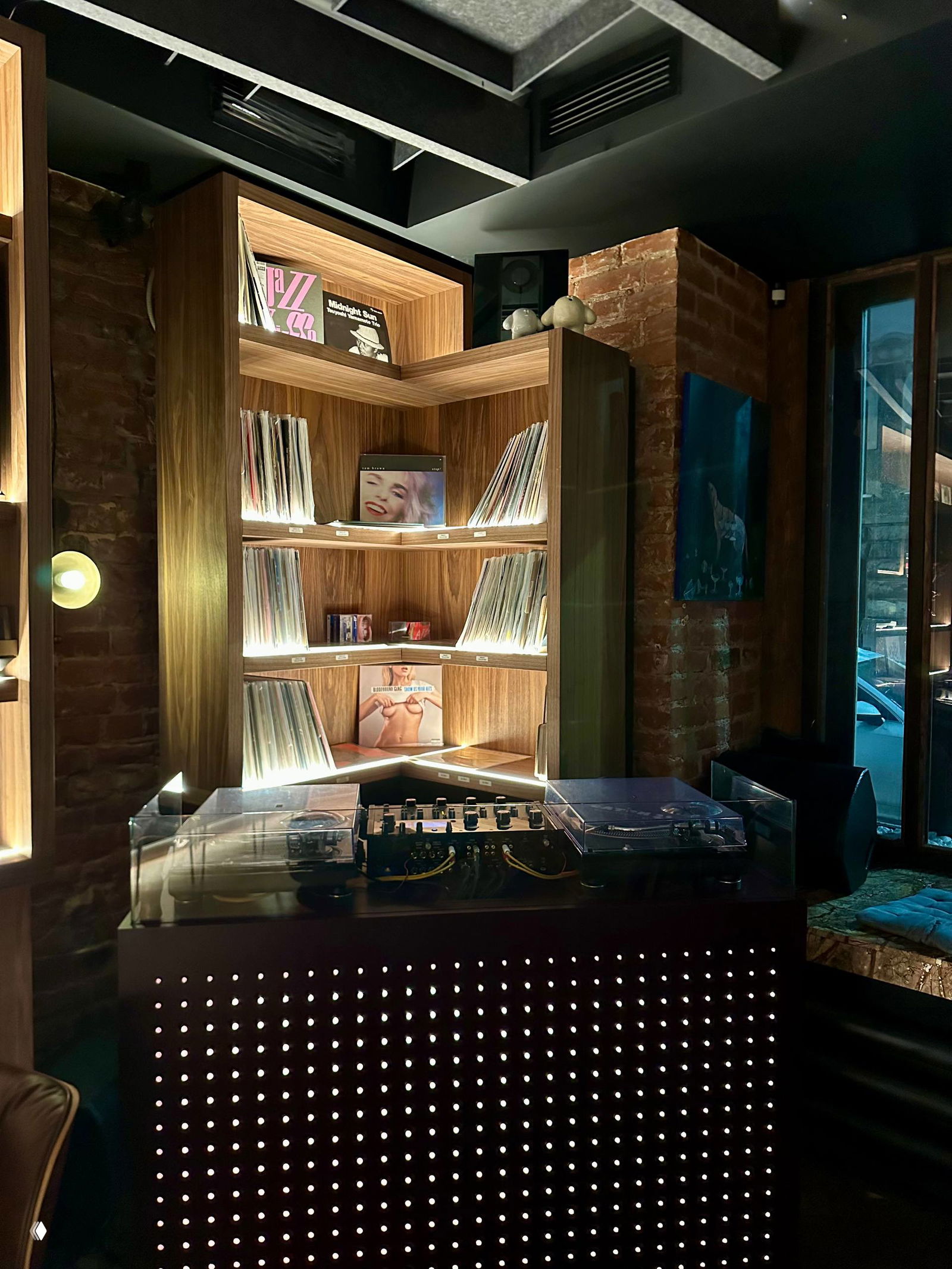 Деталь полок с виниловыми обложками и декоративными бутылками, подчёркнутая тёплой подсветкой — интерьерная экспозиция в баре