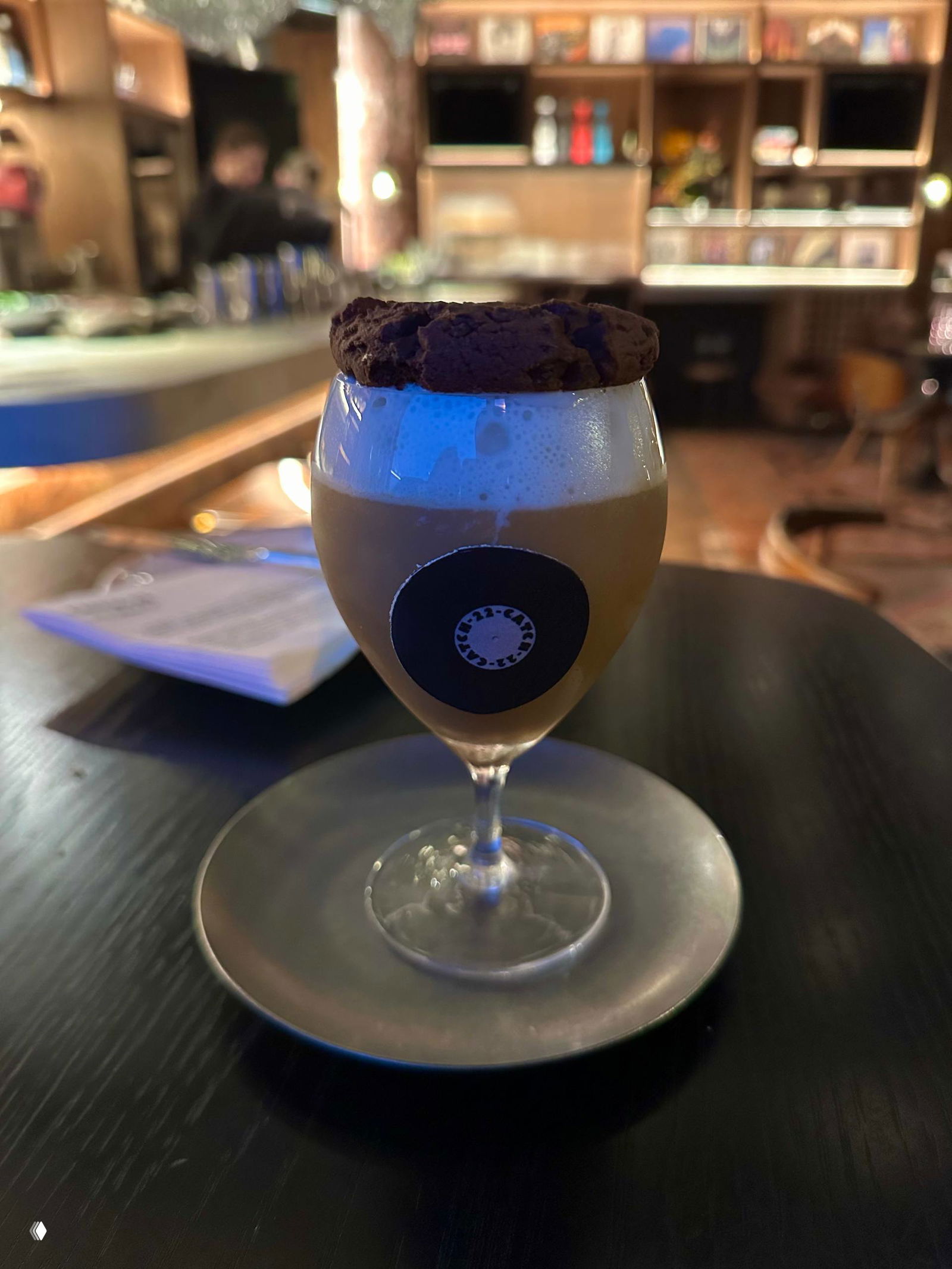 Коктейль в бокале с печеньем сверху на тёмном столе: фирменная подача напитка Catch 22 в атмосферном свете бара