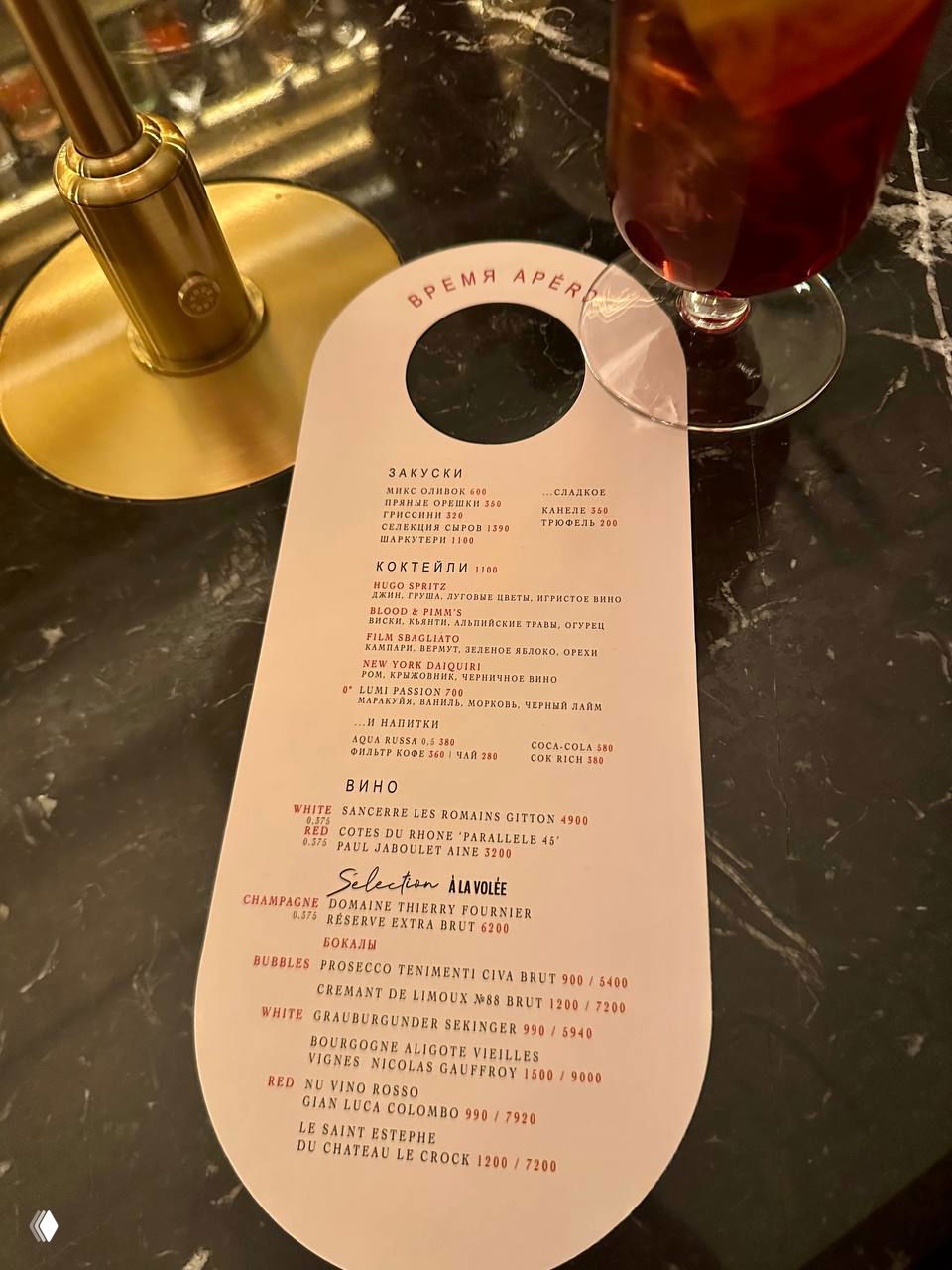 Меню аперитивов в Michele: овальная карточка с перечнем закусок, коктейлей и вин лежит на столике рядом с лампой, видно разделы и цены.