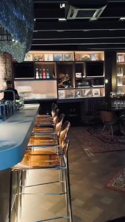 Ещё один общий вид интерьера: барная стойка с подсветкой, барные стулья и столики у окна в притемнённой атмосфере для прослушивания музыки