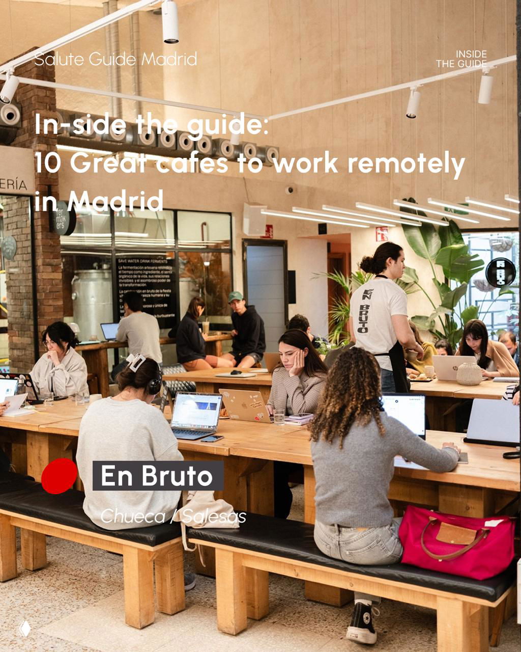 Large communal wooden table in a bustling café with people working on laptops — En Bruto workspace image in Chueca/Salesas.