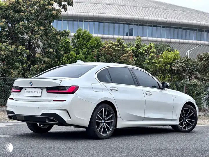 Белый BMW 3 Series 320Li M Sport, вид сзади‑сбоку на той же стоянке; демонстрация задней части, линии кузова и компоновки для пассажиров, фото объявления.