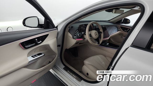 Интерьер Mercedes‑Benz E‑Class E220d 2024, бежевые кожаные сиденья, рулевое колесо Mercedes и панель приборов, вид со стороны водителя.