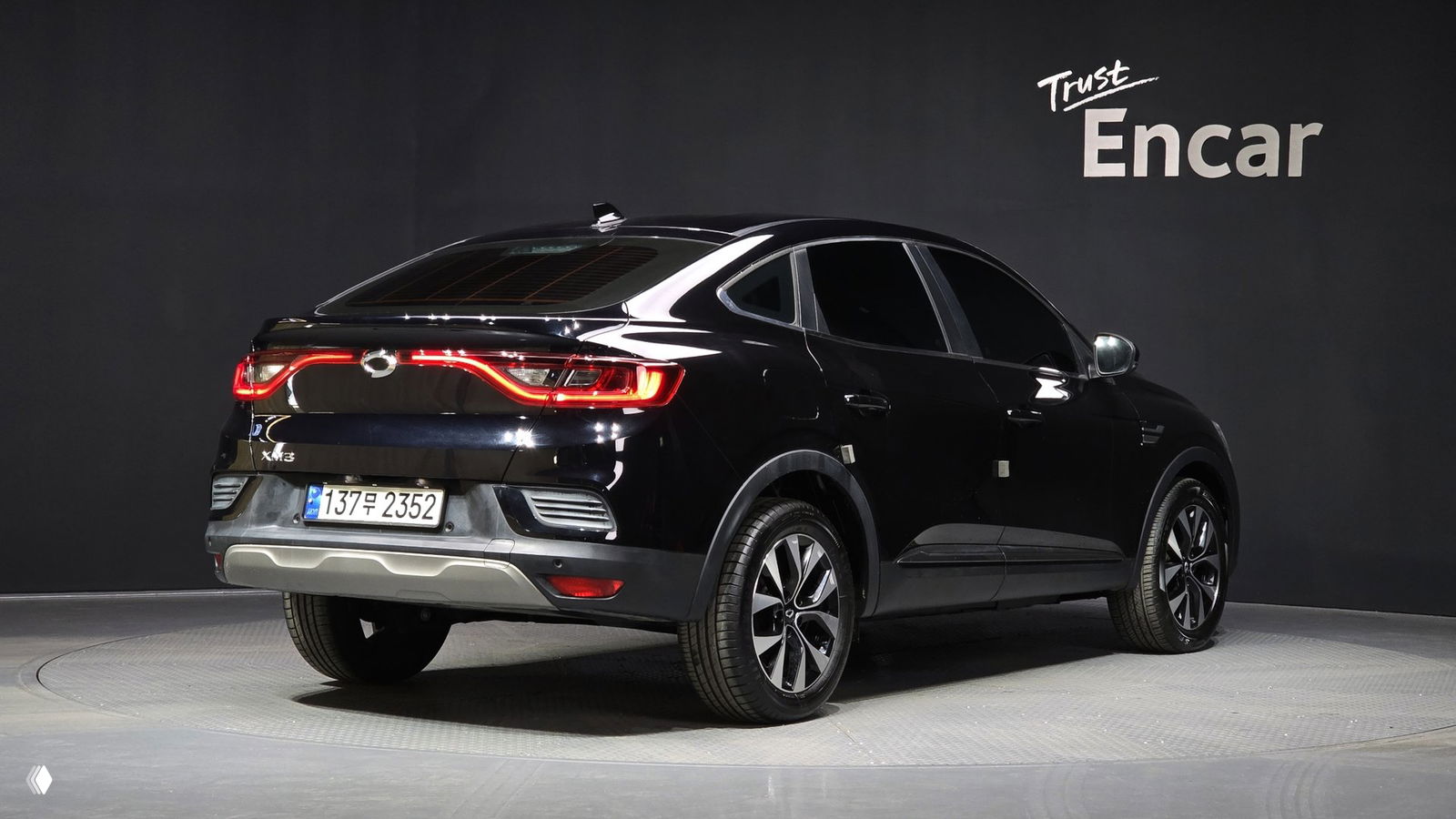 Задний трёхчетвертной вид чёрного Renault Samsung XM3 2021 года в шоуруме; видны фонари, профиль кузова и южнокорейский номерной знак.