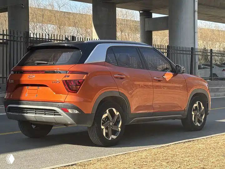 Hyundai ix25 оранжевого цвета, вид сзади и сбоку; видно багажную дверь, задние фонари и общий профиль автомобиля на улице.
