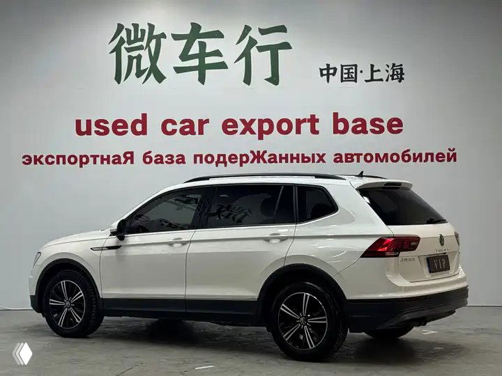 Профиль белого Volkswagen Tiguan L на стенде экспортной базы, боковой вид с литые диски и закрытые двери.