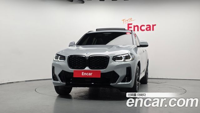 Фронтальный план BMW X4 xDrive20i M Sport 2022 в шоуруме Encar — крупный вид решётки радиатора, бампера и дизайн‑линий передней части автомобиля.