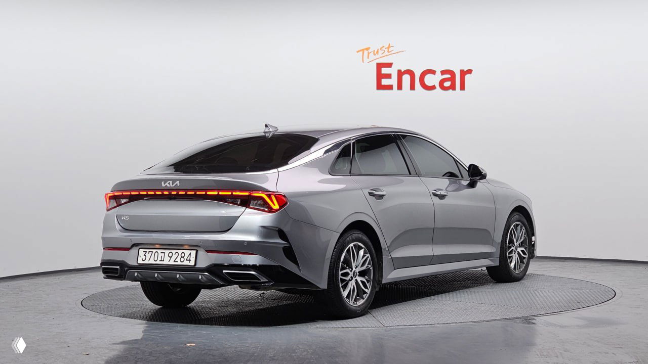 Задняя трёхчетвертная проекция серебристого Kia K5 в шоуруме Encar: задние фонари, форма багажника и номер автомобиля видны.