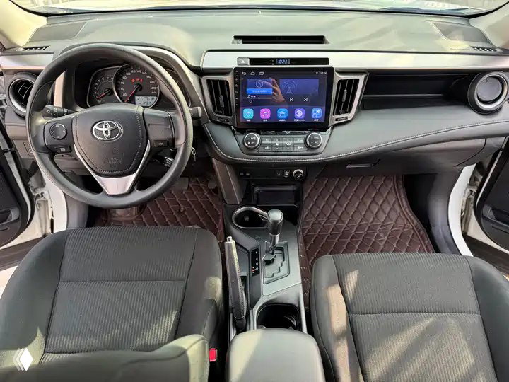 Салон Toyota RAV4 2019: центральная консоль с мультимедиа-экраном, руль, рычаг вариатора и чистые тканевые передние сиденья.