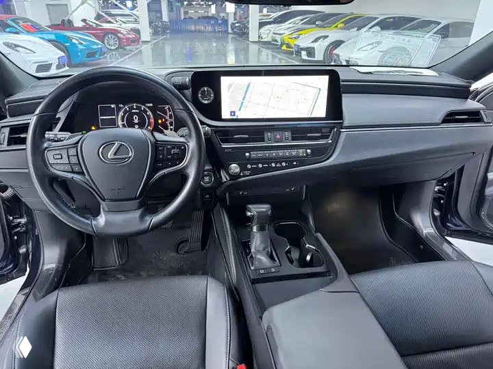 Интерьер Lexus ES 200 2022: руль с логотипом Lexus, мультимедийный дисплей и центральная консоль — общий вид салона и приборной панели.