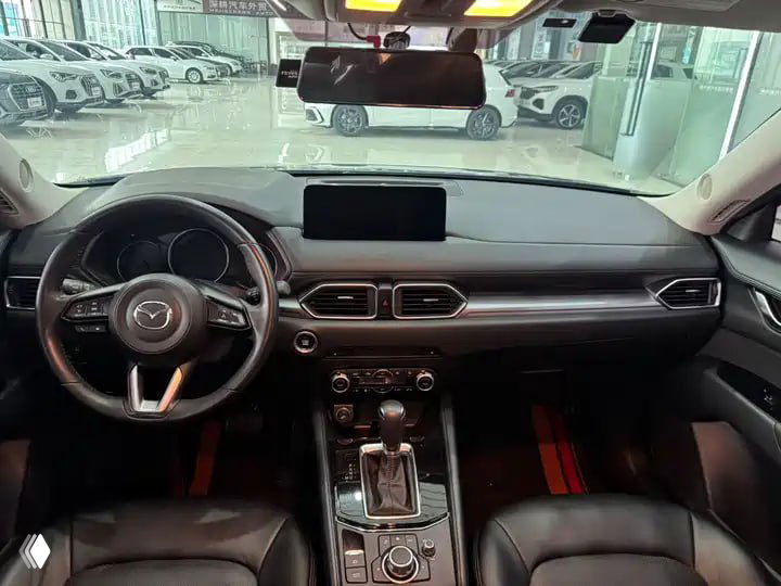 Салон Mazda CX-5 2023: панель приборов, руль и центральная консоль с мультимедийным экраном и селектором коробки передач в хорошо освещённом шоуруме.