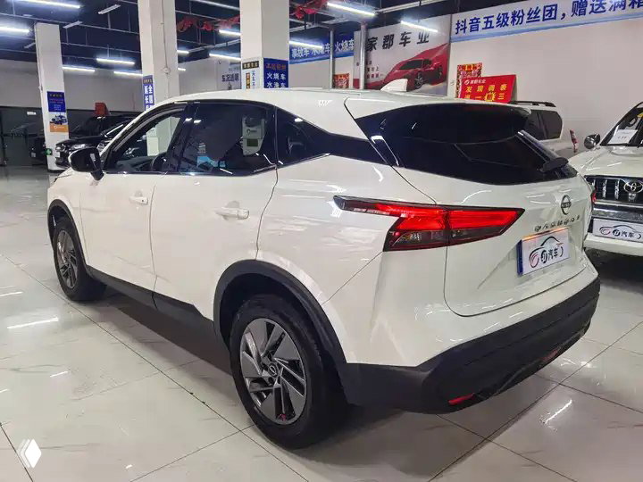 Боковой и задний вид белого Nissan Qashqai 2023 в выставочном зале: багажная часть и оптика, автомобиль выставлен на демонстрацию в китайском автосалоне.