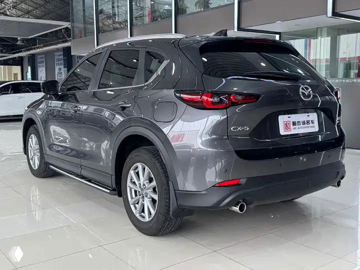 Задняя часть серой Mazda CX-5 2023 в автосалоне, вид на фонари, багажник и задний бампер, автомобиль стоит на белом полу шоурума.