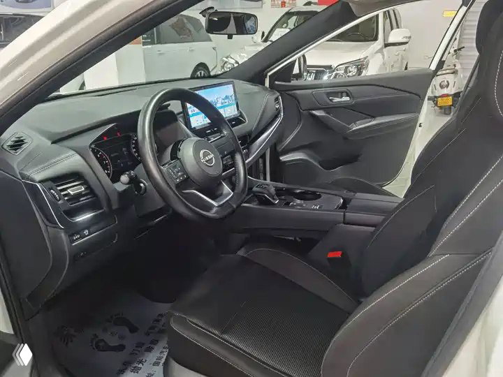 Интерьер Nissan Qashqai 2023: приборная панель, мультимедийный дисплей, центральная консоль и передние сиденья, фото сделано в дилерском зале в Китае.