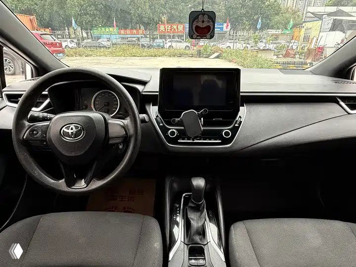 Салон Toyota Corolla: передняя панель, руль, центральный экран и селектор коробки CVT, вид с места водителя в исходном состоянии.