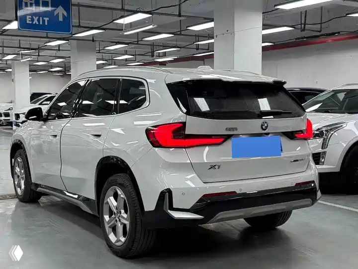 Задняя часть BMW X1 sDrive20Li: багажник, задние фонари и профиль автомобиля на крытой стоянке; фото демонстрирует состояние кормовой части для проверки.