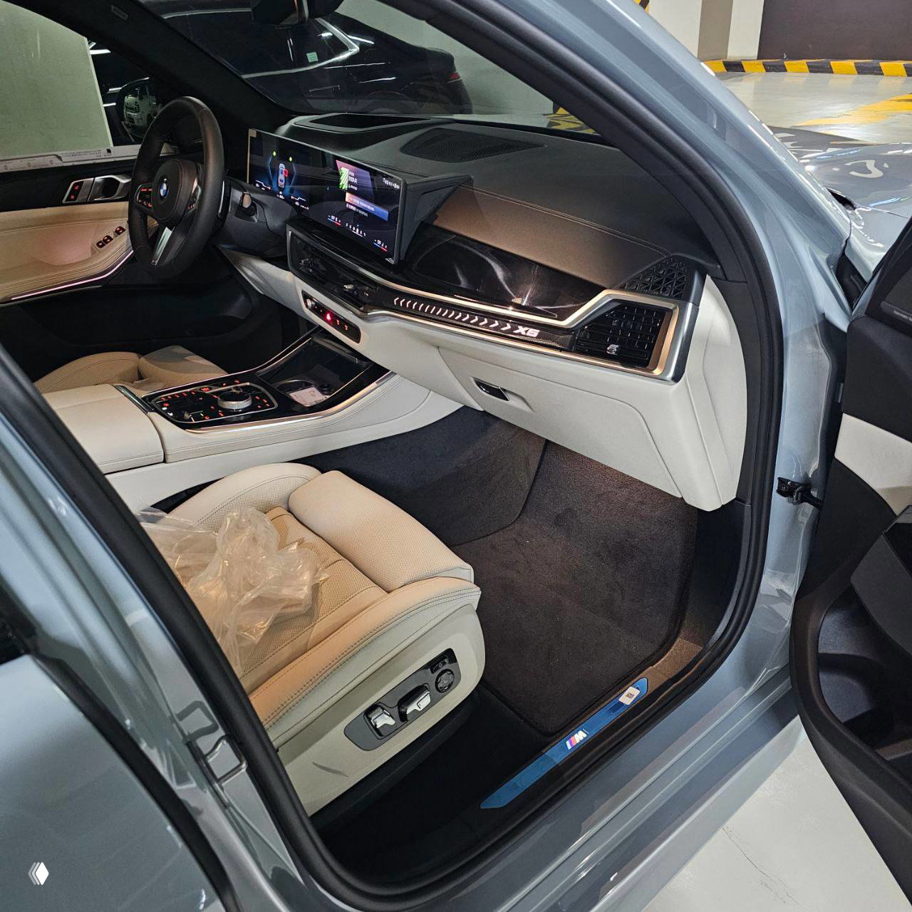 Салон BMW X5 2026: передняя панель, белая кожаная отделка, центральная консоль и цифровая приборная панель, вид на водительское место.