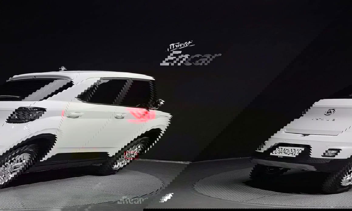 Белый Hyundai Venue 2023 (1.6 Premium) в шоуруме Encar: задний трёхчетвертный ракурс, видна кормовая часть, багажник, эмблема и корейский номерной знак.