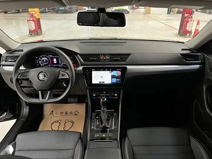 Интерьер Skoda Superb 2024: цифровая приборная панель, центральный экран с CarPlay, руль и передние сиденья в чёрной отделке.