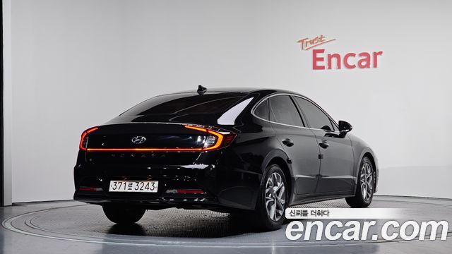 Чёрный Hyundai Sonata 2021 в шоуруме, вид сзади под углом; заметна светящаяся светодиодная полоска задних фонарей и фон с логотипом Encar.