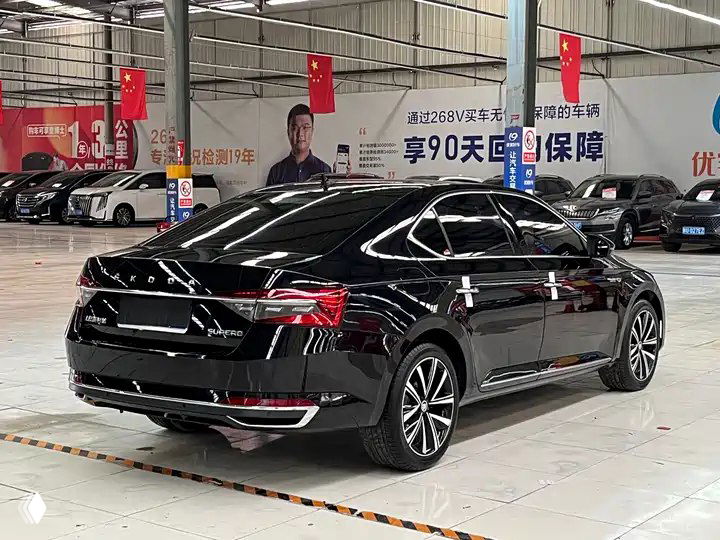 Задняя часть чёрного Skoda Superb 2024 в автосалоне, видно форму багажника, задние фонари и общий профиль автомобиля в стойке осмотра.