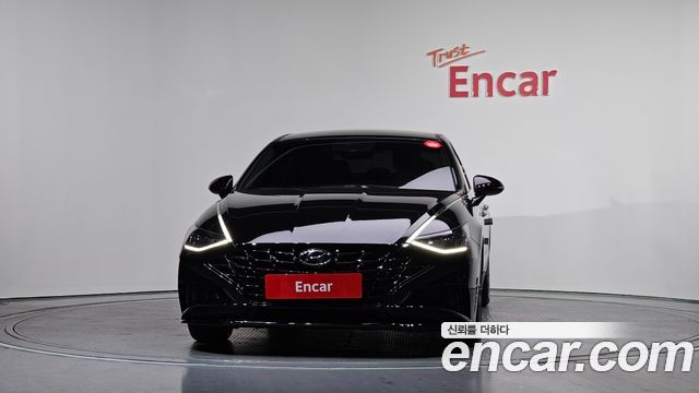 Hyundai Sonata 2021 чёрного цвета, фронтальный вид в шоуруме; выразительные фары и центральная красная табличка с логотипом дилера Encar.