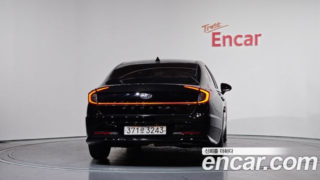 Задняя часть Hyundai Sonata 2021 чёрного цвета в шоуруме, вид по центру; видно оформление фонарей, номерную табличку и бренд Encar на стене.