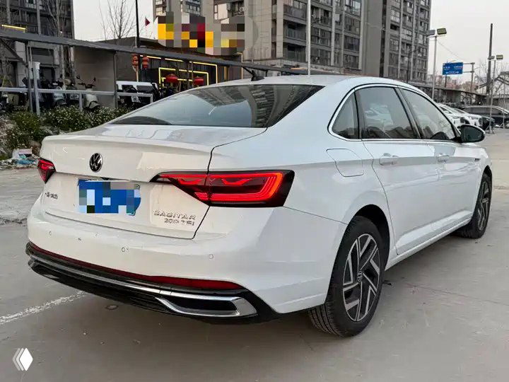 Задний план белого Volkswagen Sagitar 200TSI 2023: видны фонари, эмблема и бампер на фоне многоэтажек и парковки, номера замазаны.