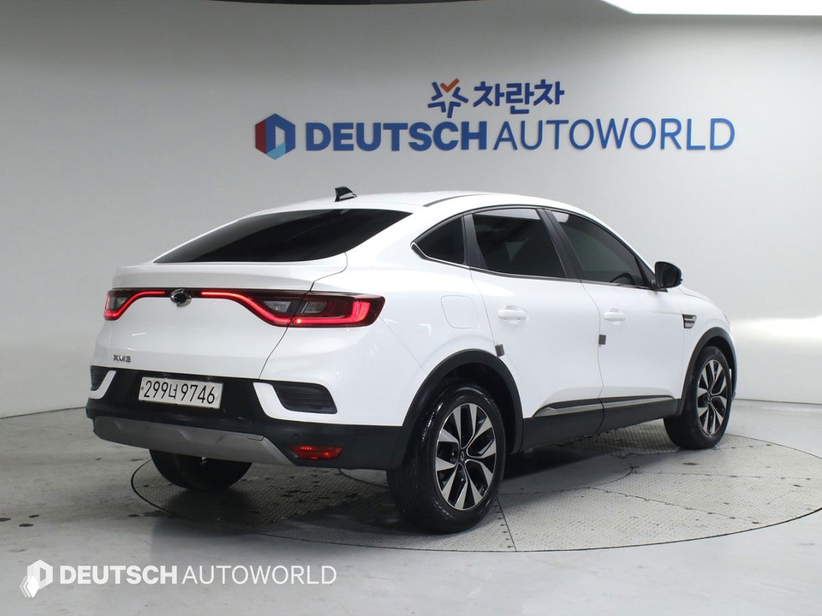 Задний трёхчетвертной ракурс белого Renault XM3 в шоуруме, подчёркнута купе‑линия крыши и световая вставка задних фонарей на фоне стенда Deutsch Autoworld.