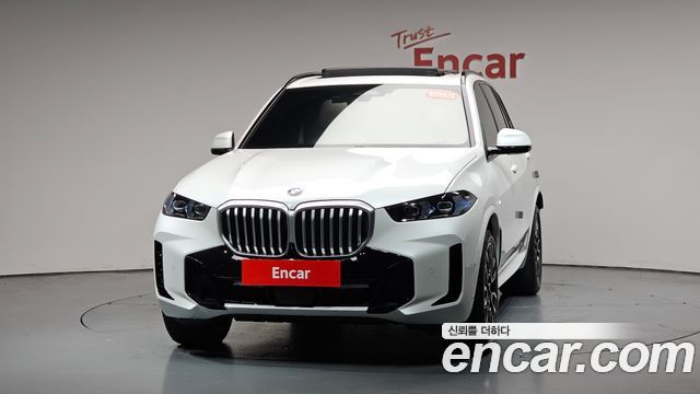 Фронтальный вид белого BMW X5 xDrive 30d M Sport в студийном зале Encar; видна фирменная решётка радиатора и передняя оптика.