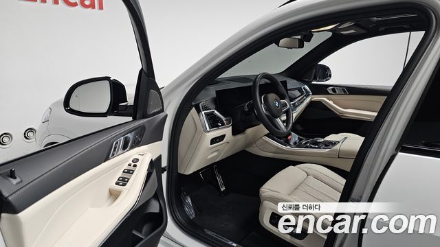 Интерьер BMW X5 xDrive 30d M Sport: передняя панель, руль и передние сиденья бежевого цвета, акцент на отделке и центре управления.