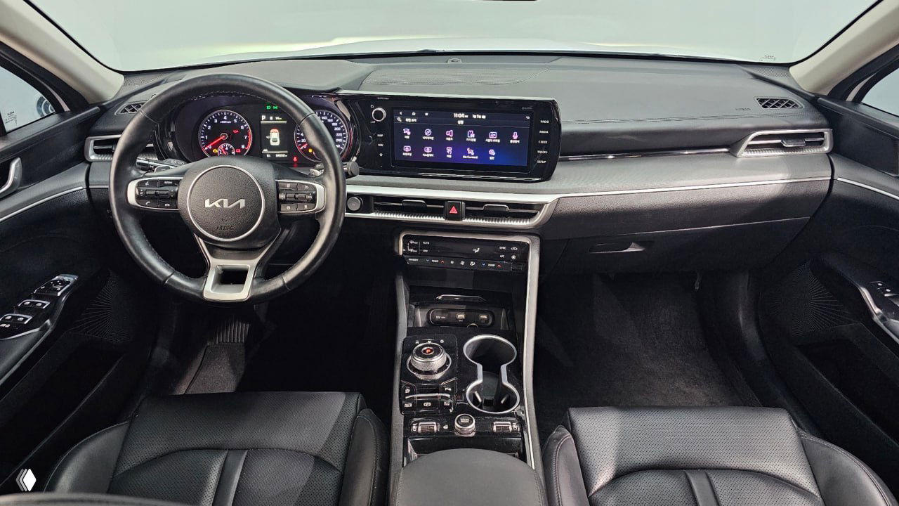 Интерьер KIA K5: панель приборов, руль с логотипом KIA и большой центральный сенсорный экран, вид на центральную консоль и ручку селектора.