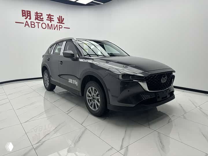 Диагональный ракурс Mazda CX-5 2.0L Pro 2026: вид кузова, колёс и отражения потолочных светильников на глянцевом лаке автомобиля.