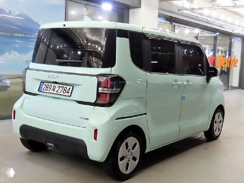 Задняя часть салатового Kia Ray Van в автосалоне, крупный план заднего бампера, фон витрины и корейский номер на багажнике