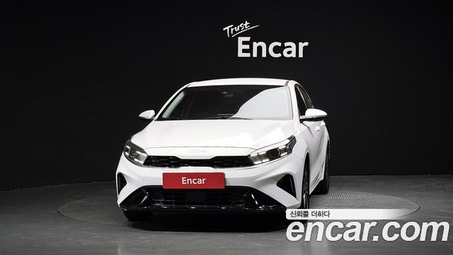 Крупный план передней части белого Kia K3 2022, видна решётка радиатора и фирменный логотип на тёмном фоне студии Encar.