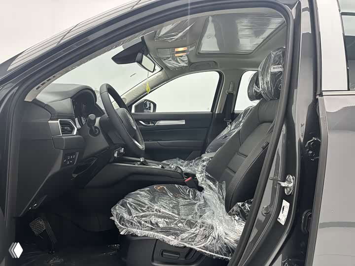 Интерьер Mazda CX-5 2026: водительское сиденье с защитной плёнкой, руль и центральная консоль видны на фото салона дилерского автомобиля.