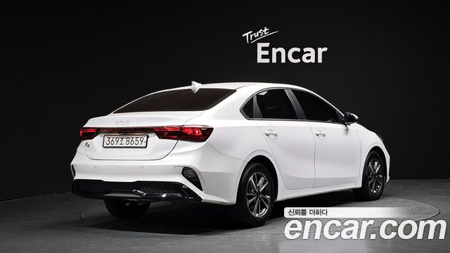 Кадр сзади белого Kia K3 2022 в студийном помещении Encar; видна задняя оптика и номер на выставочной площадке.