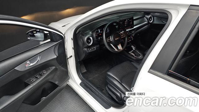 Фотография салона Kia K3 2022: открытая дверь, руль, приборная панель и переднее сиденье в интерьере автомобиля.