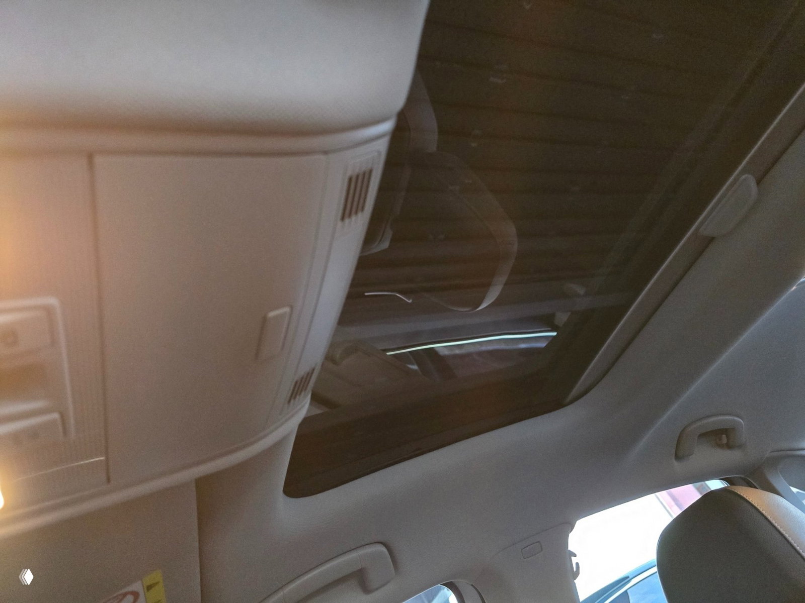 Крупный план салонной части потолка с панорамной крышей: стеклянный люк, светлая обивка потолка, плафон и рукоятки, интерьерный вид сверху.