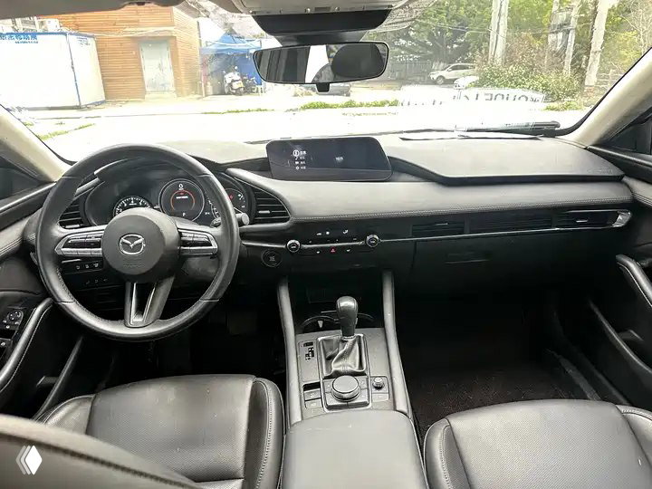 Интерьер Mazda3 Axela: руль, панель приборов и центральная консоль с монитором и селектором автомата; чёрная отделка салона.