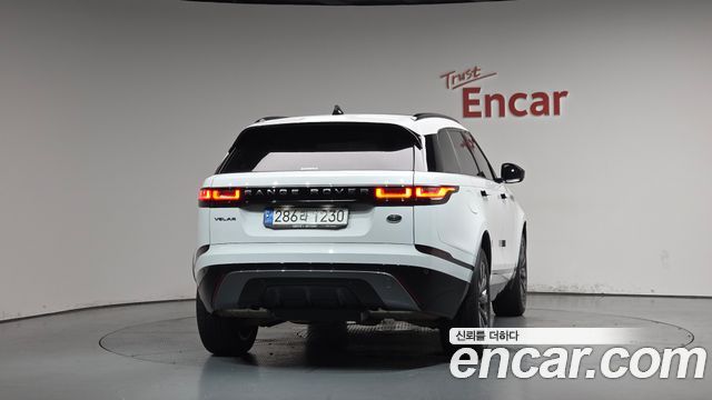 Задний центральный вид белого Range Rover Velar на поворотном подиуме Encar, видна задняя оптика, бампер и номер, студийная подсветка