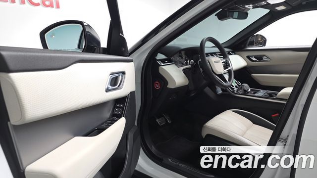 Интерьер Land Rover Range Rover Velar: открытая дверь водителя, передняя панель, руль и салон светлой отделки, видна компоновка приборной панели и кресла